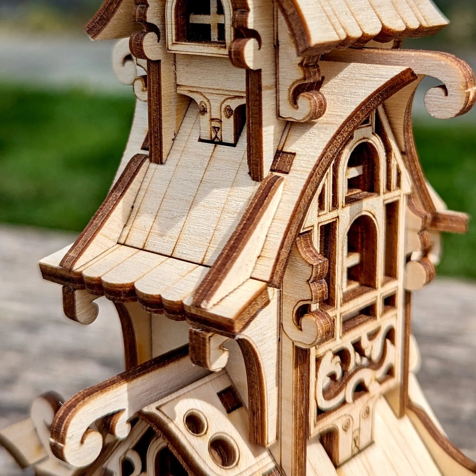 Wooden model of a detailed house with intricate carvings against a blurred natural background