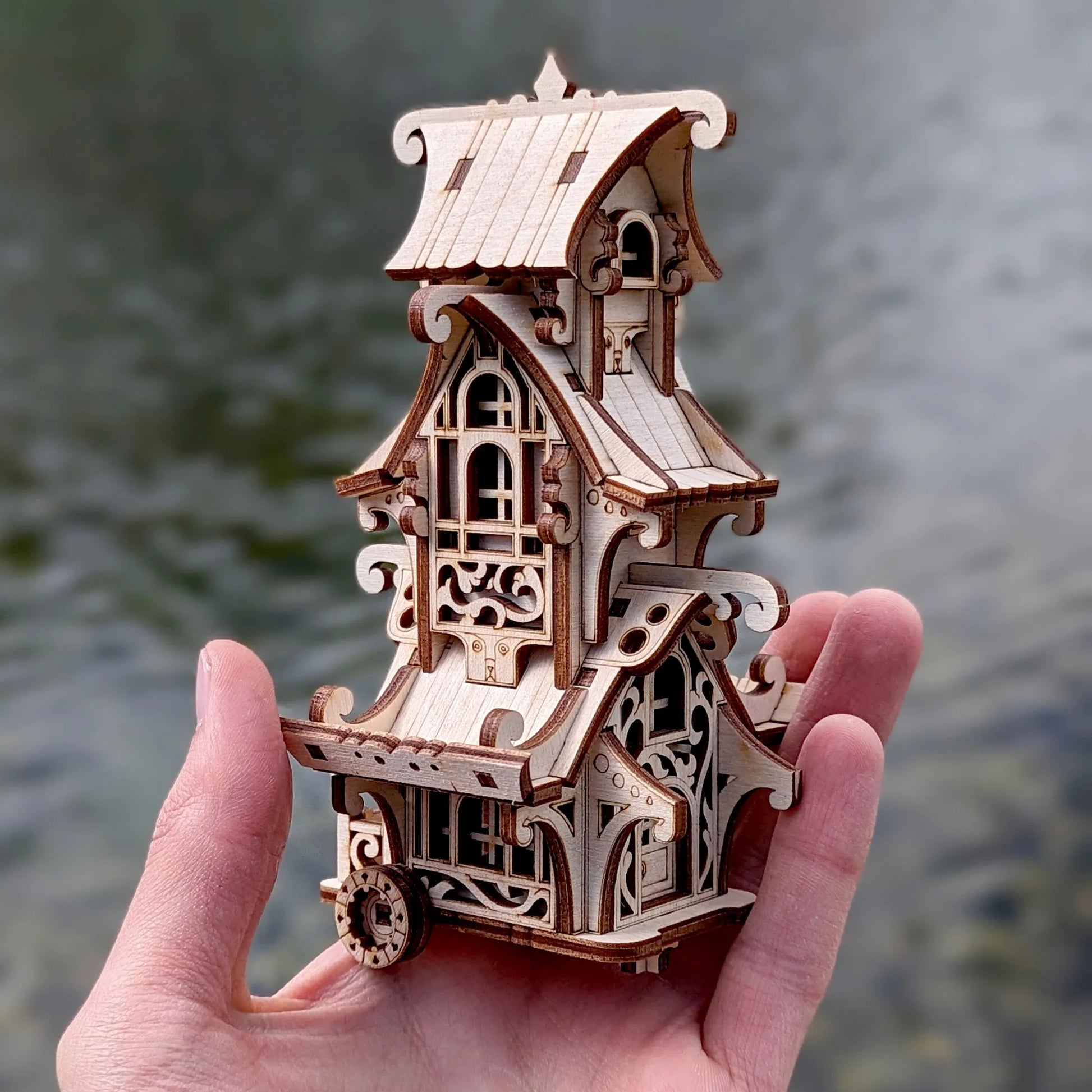 Hand holding a intricately designed wooden model of a house against a blurred natural background