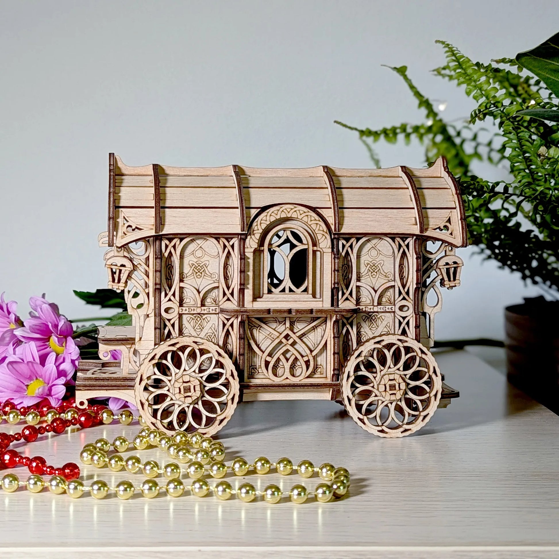 Wooden model of a caravan wagon with intricate designs on a surface with flowers and beads.