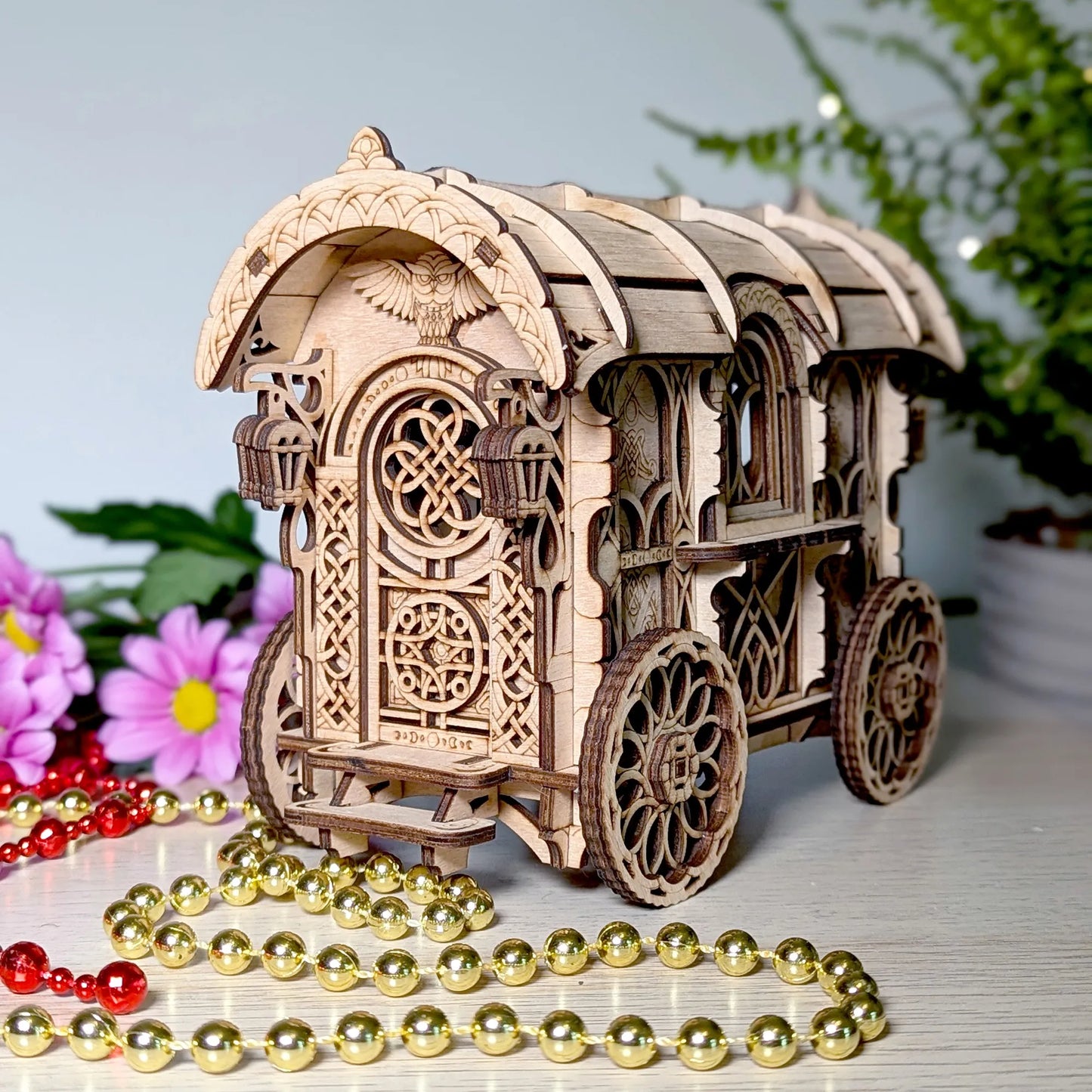 Wooden model of a decorative carriage with intricate designs, surrounded by flowers and beads on a light surface.