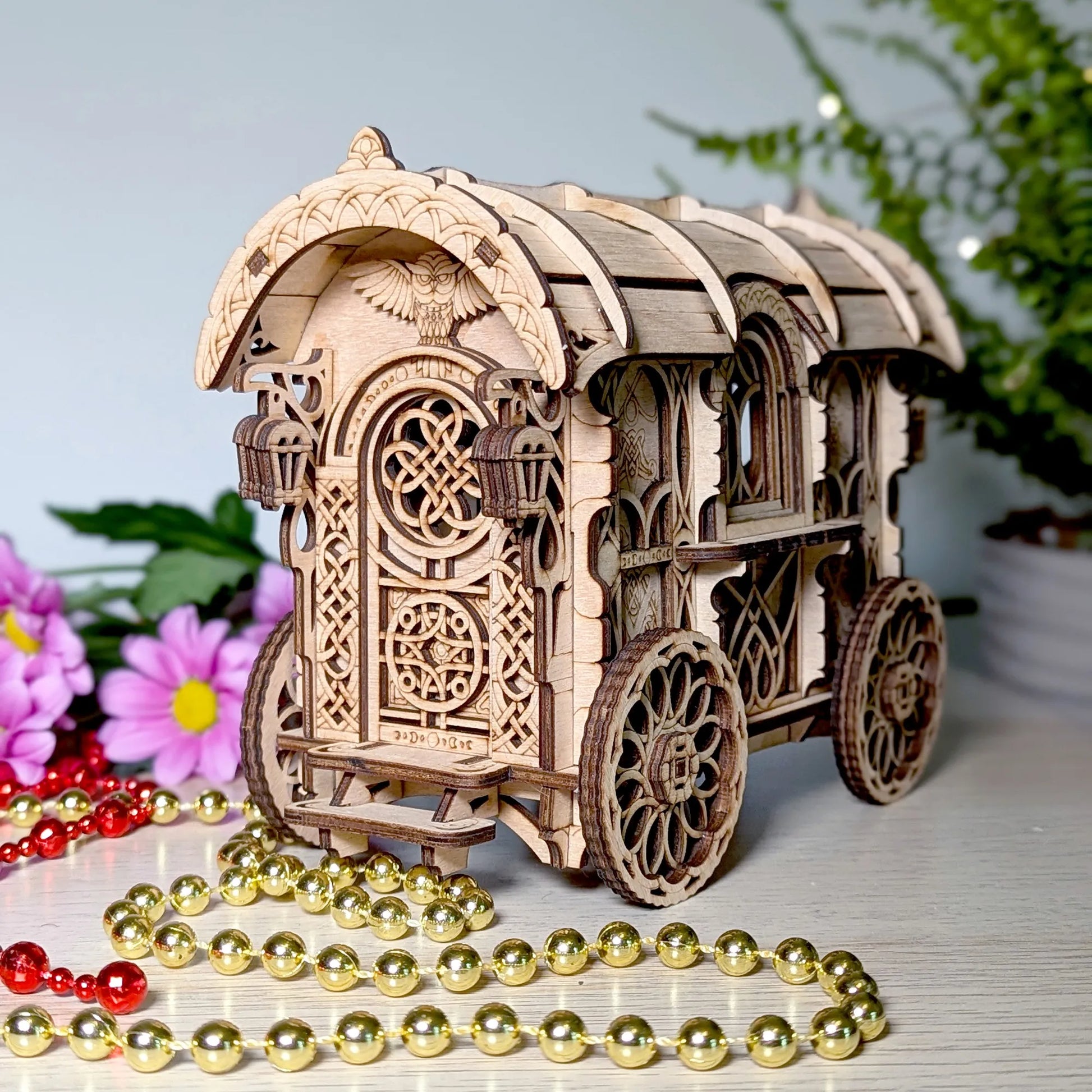 Wooden model of a decorative carriage with intricate designs, surrounded by flowers and beads on a light surface.
