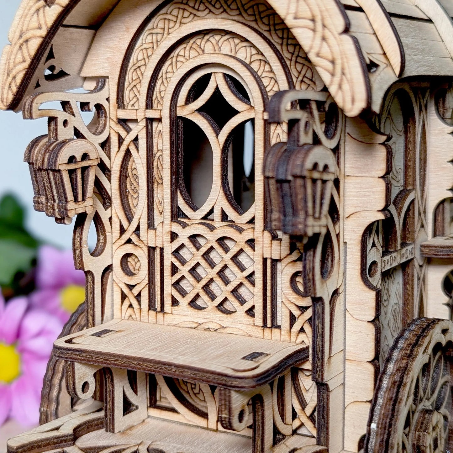 Wooden model of a carriage with intricate designs and wheels, set against a blurred floral background.