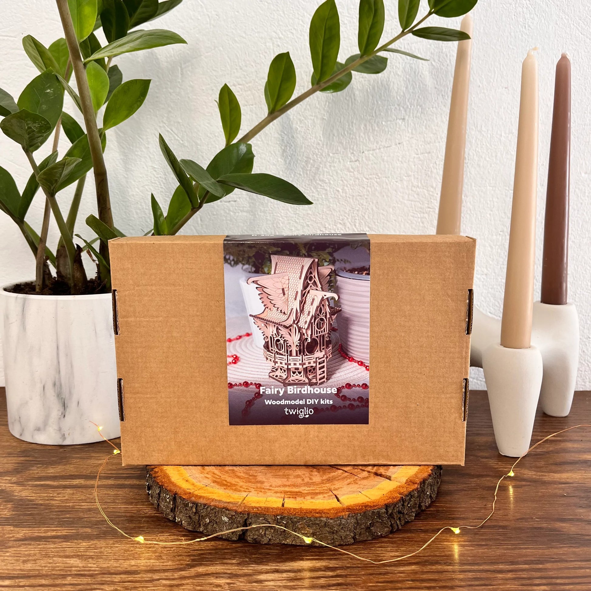 Wooden DIY kit box for fairy birdhouse on a wooden surface with candles and a plant in the background.