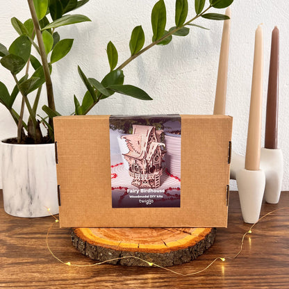 Wooden DIY kit box for fairy birdhouse on a wooden surface with candles and a plant in the background.