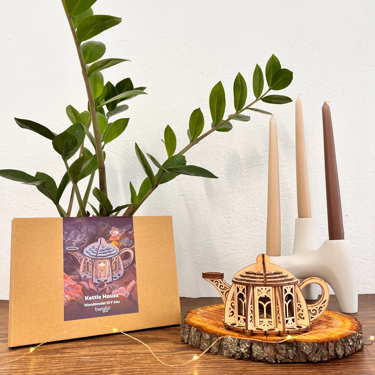 Wooden teapot model on a wooden stand with candles and a plant in the background