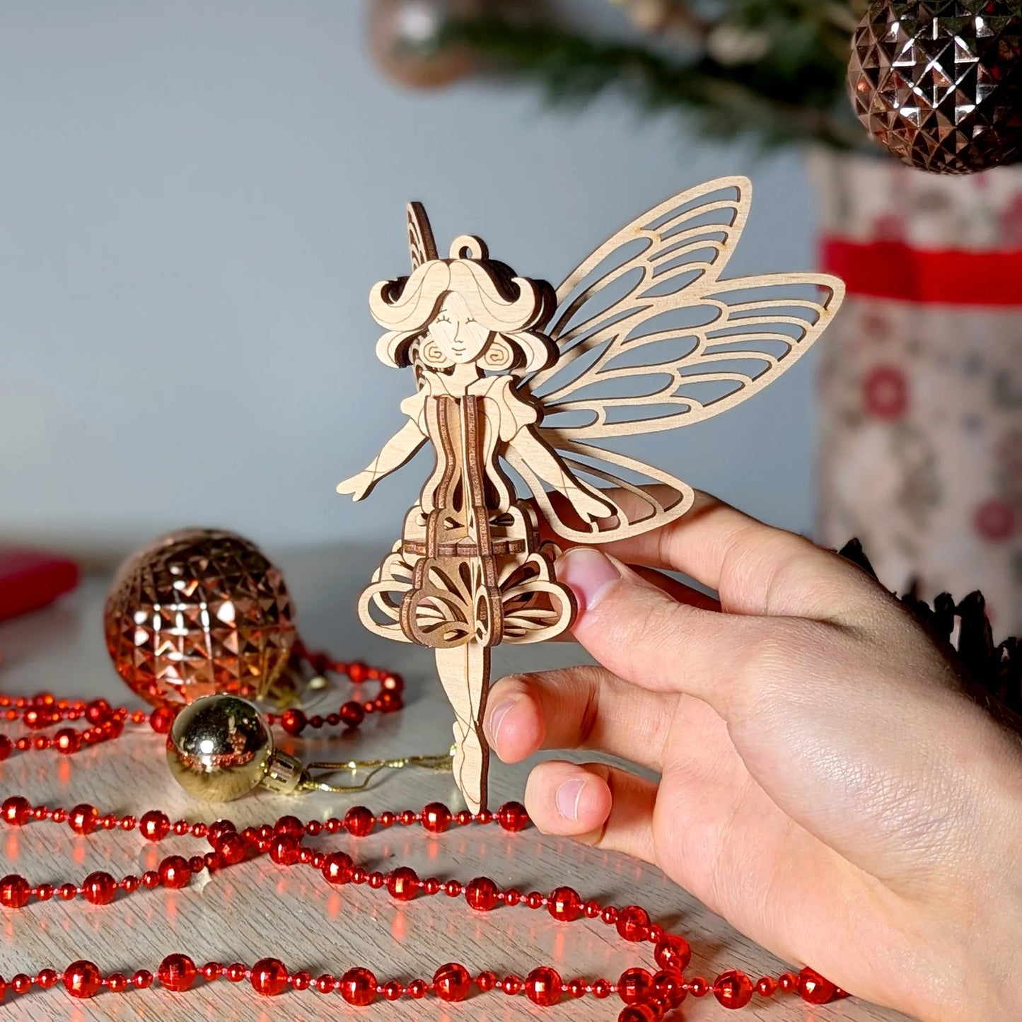 Wooden fairy ornament held by a hand with Christmas decorations in the background