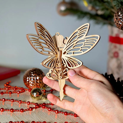 Hand holding a decorative fairy 
ornament with Christmas decorations in the background
