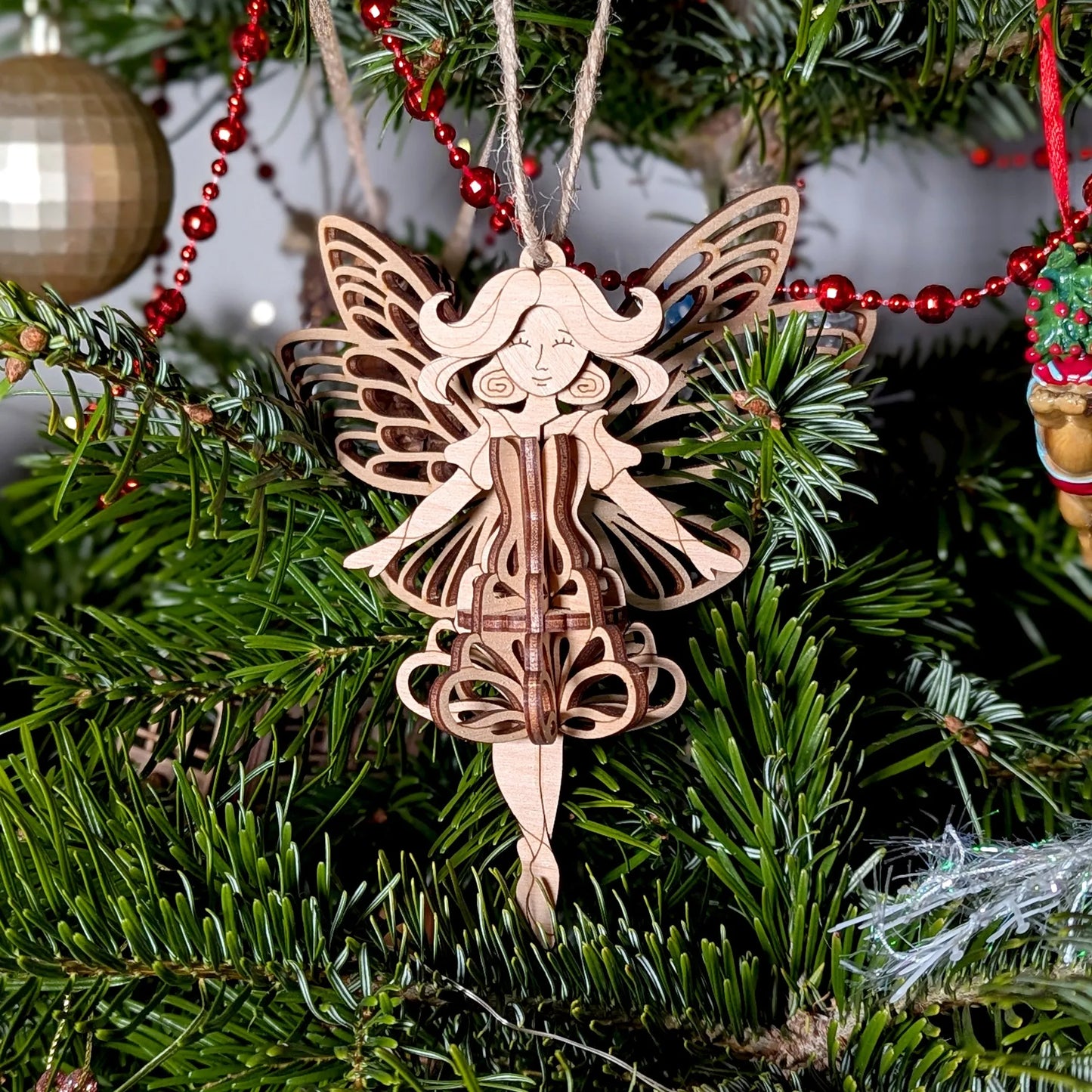 Wooden fairy ornament hanging on a Christmas tree with red beads.