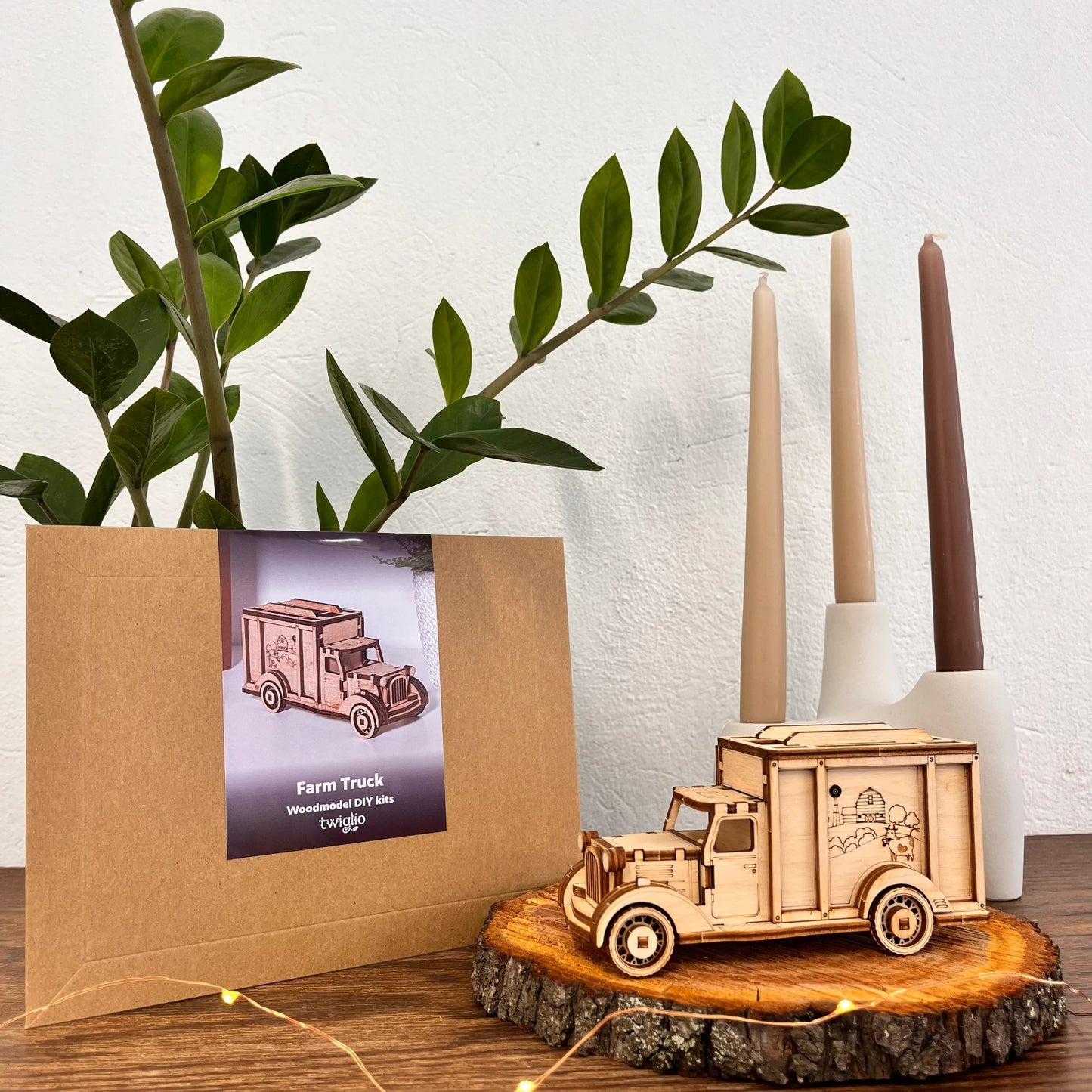 Wooden farm truck model on a wooden surface with a plant and candles in the background