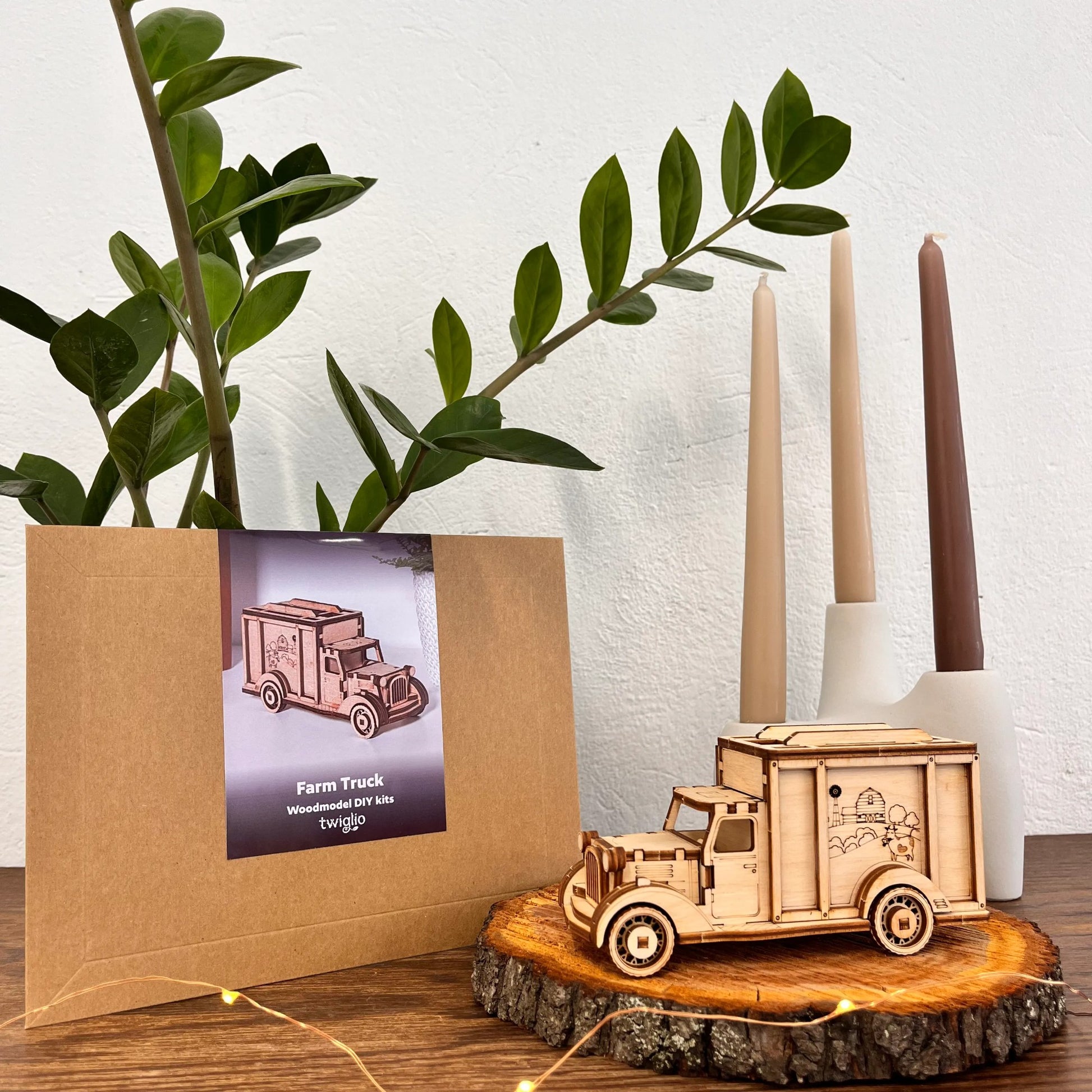 Wooden farm truck model on a wooden surface with a plant and candles in the background