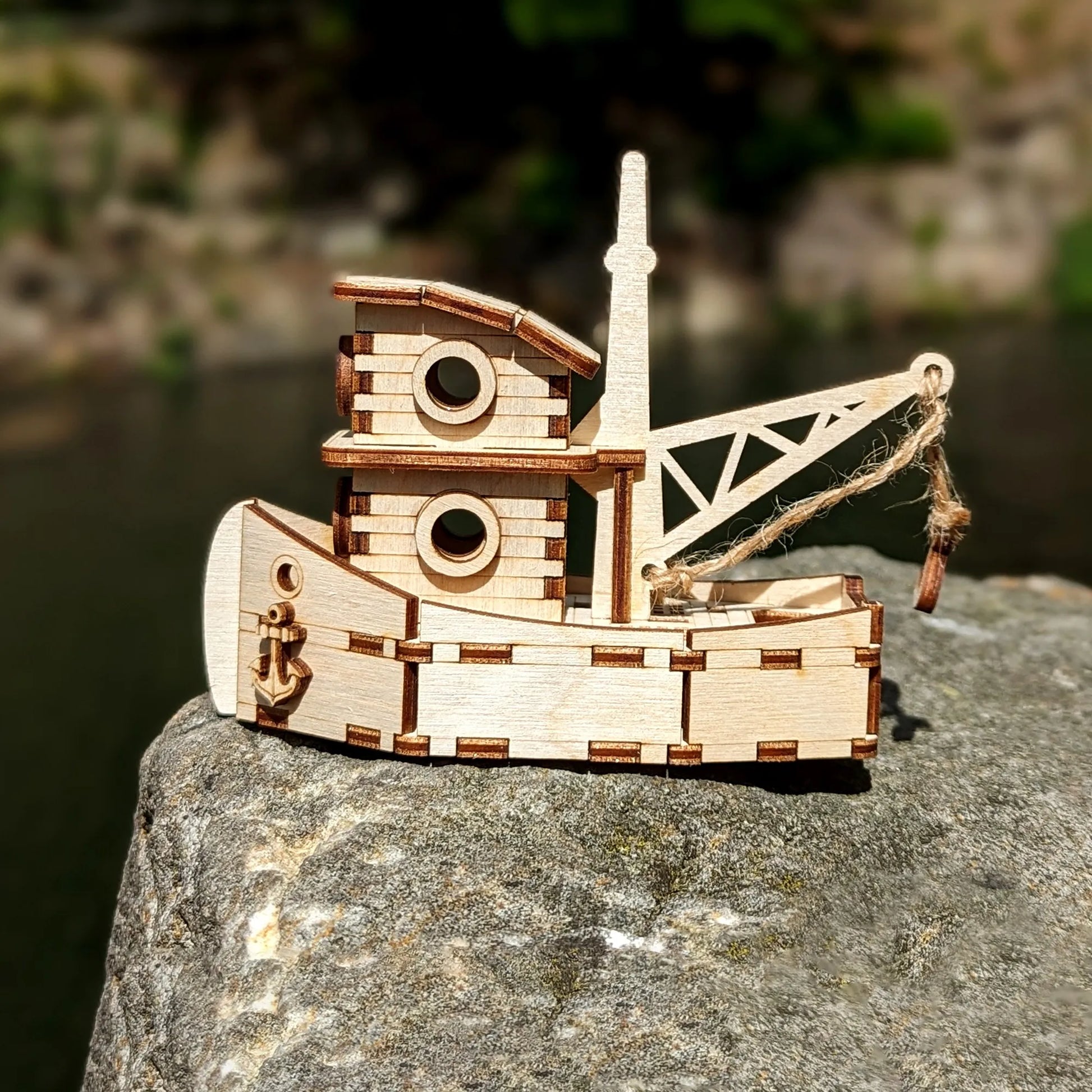 Wooden toy boat with crane on a rock by a body of water