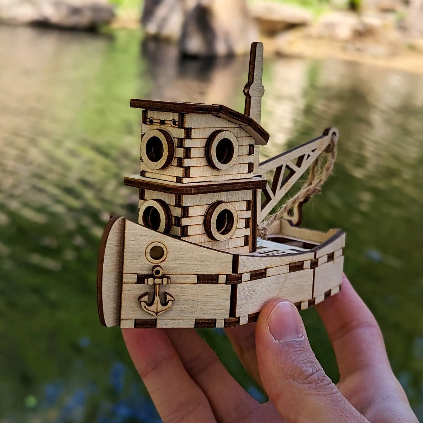 Wooden toy boat model held by a hand with a blurred natural background
