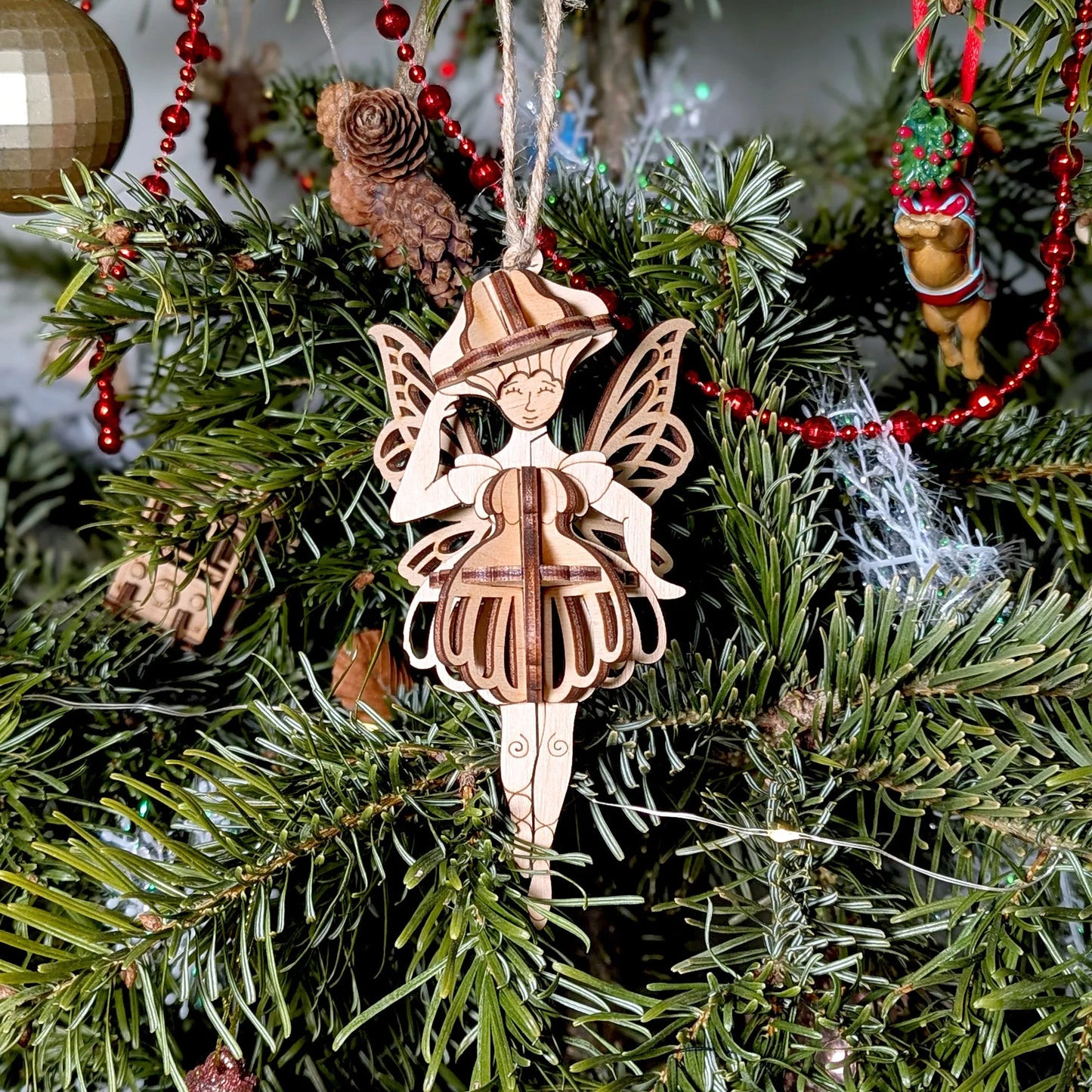 Wooden fairy ornament on a Christmas tree with red beads and pine cones.
