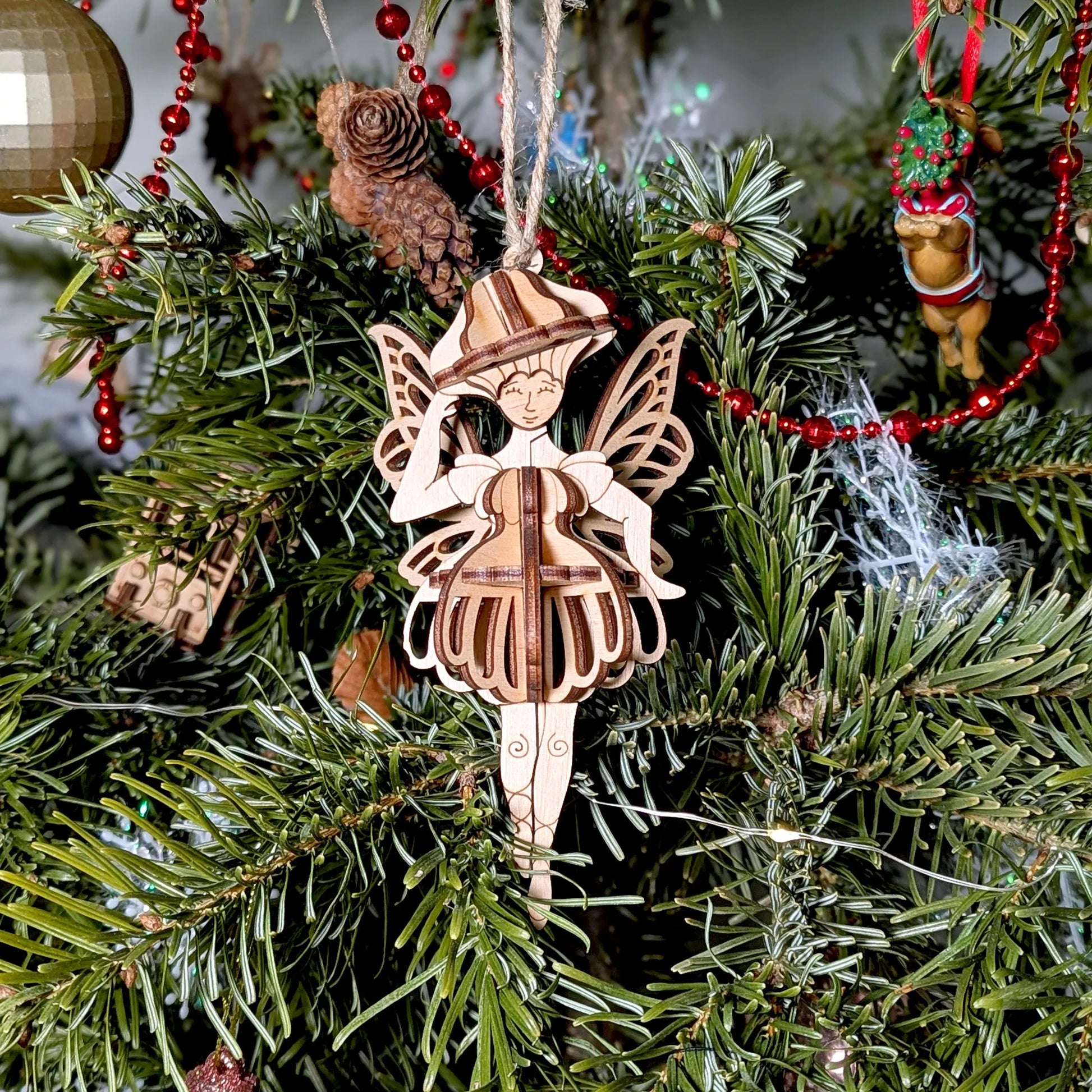 Wooden fairy ornament on a Christmas tree with red beads and pine cones.