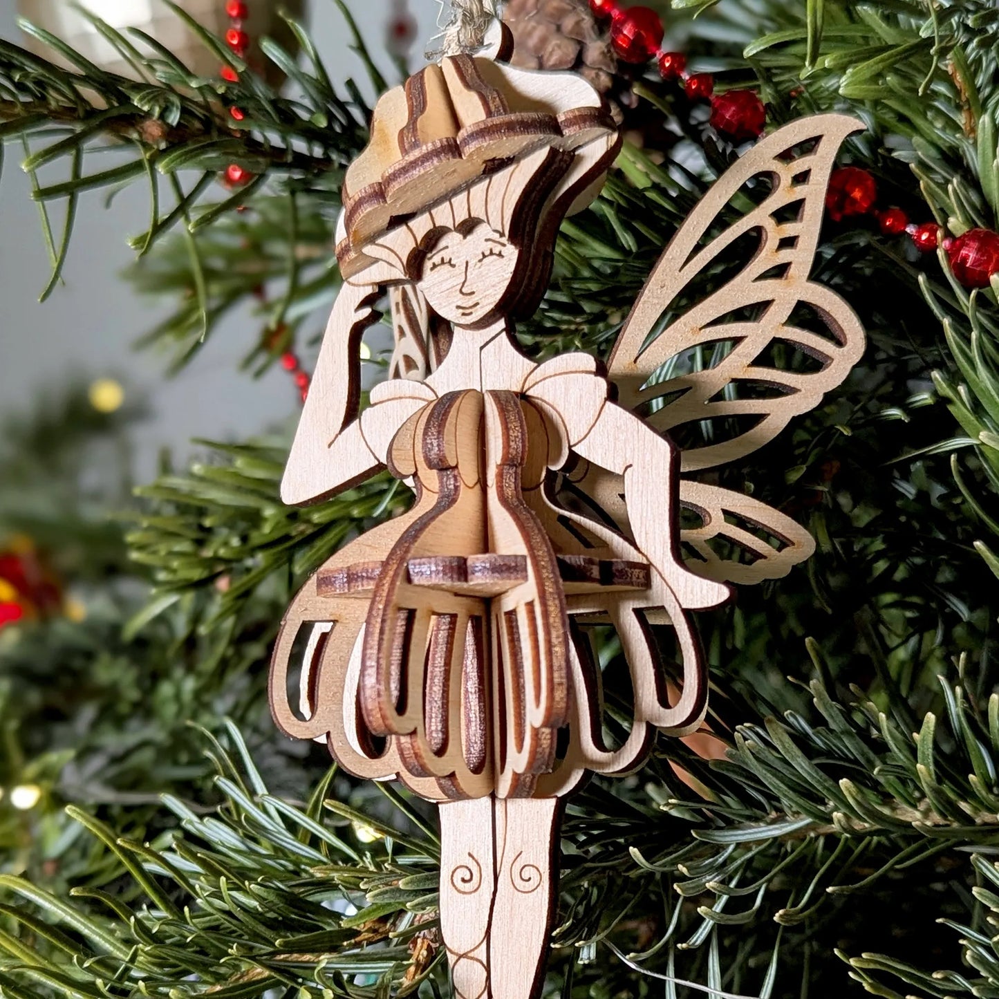 Wooden fairy ornament on a Christmas tree with green leaves and red berries.