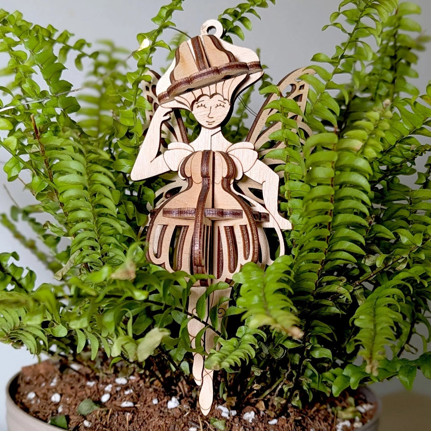 Wooden decorative figure of a girl playing a violin in a potted fern plant.