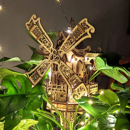 Decorative wooden windmill with intricate details, surrounded by green leaves and string lights.