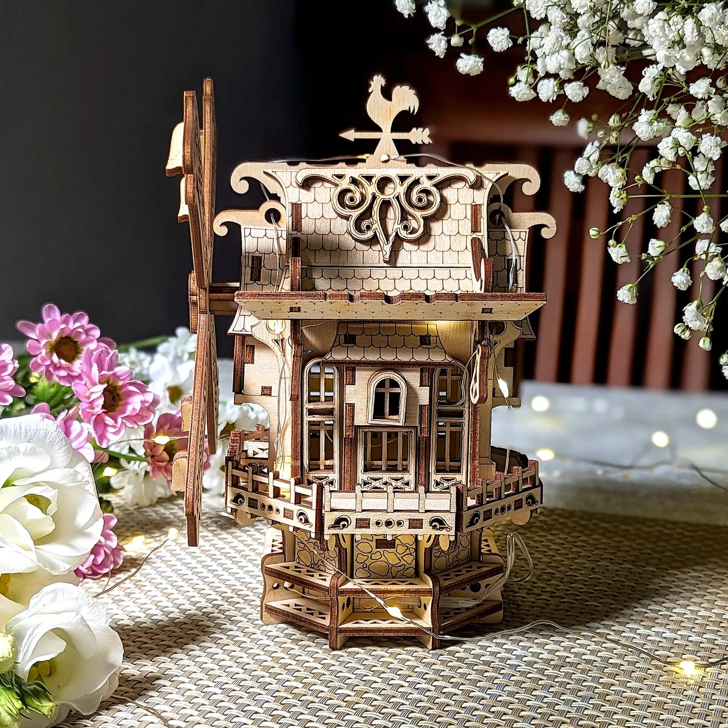 Wooden model of a windmill with decorative elements on a table with flowers.