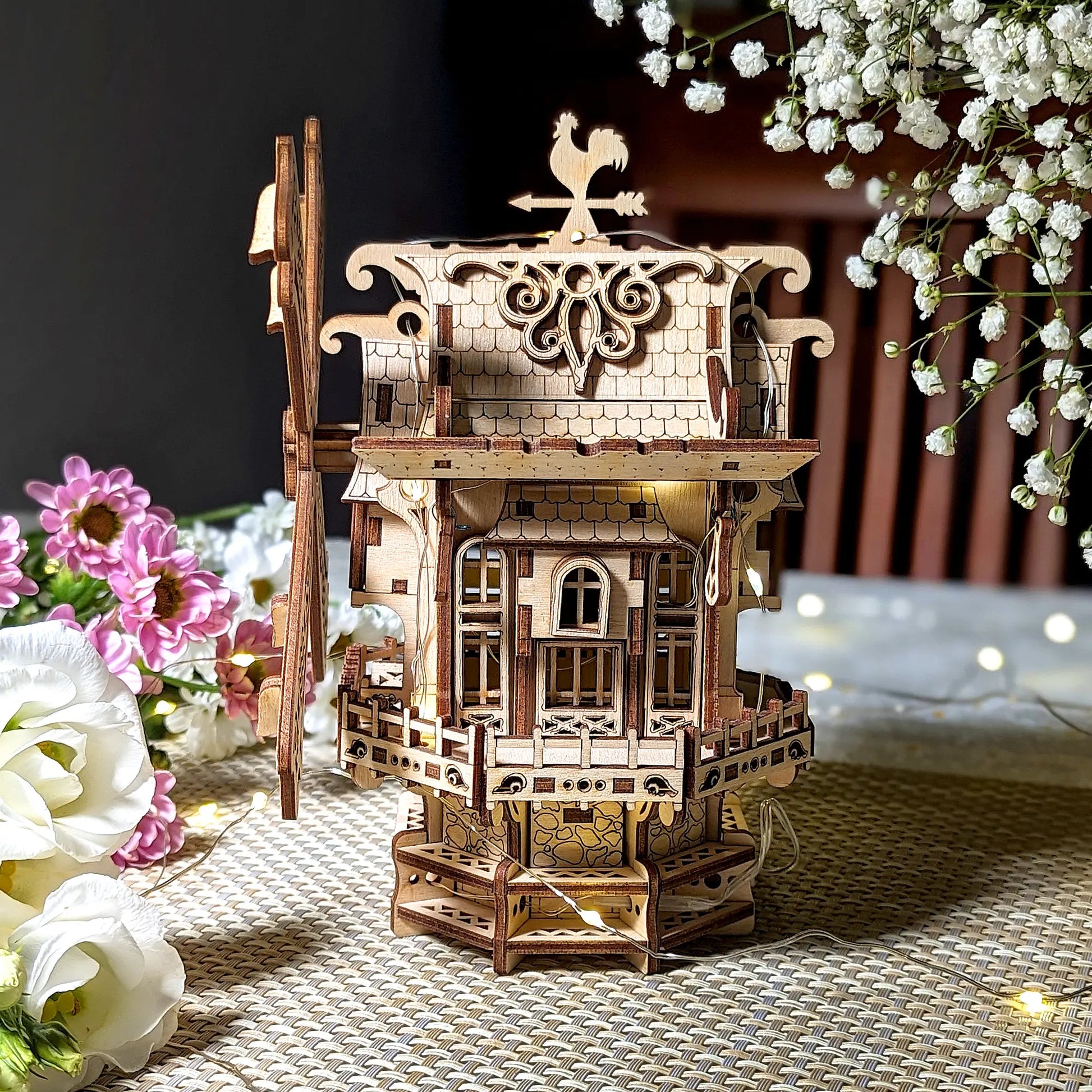 Wooden model of a windmill with decorative elements on a table with flowers.
