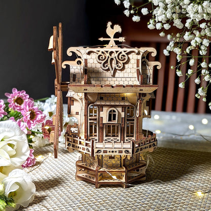 Wooden model of a windmill with decorative elements on a table with flowers.