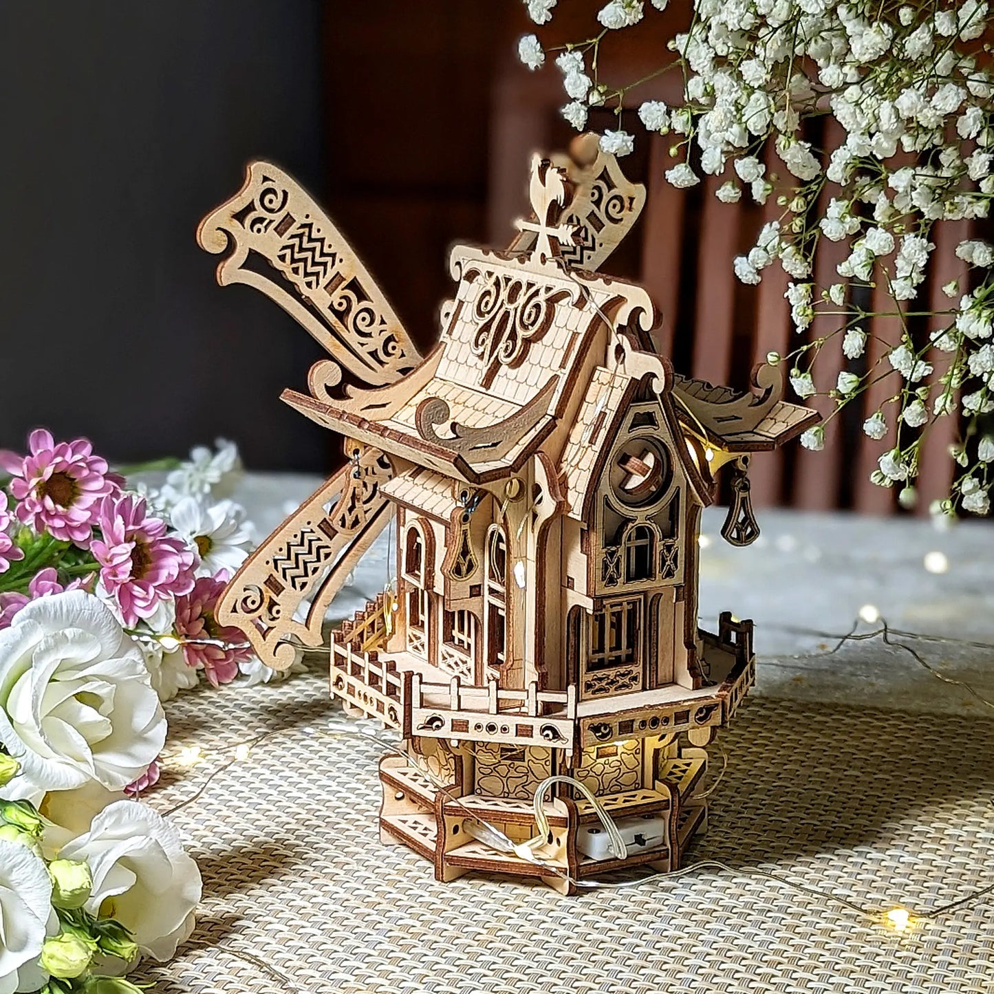 Wooden model of a windmill with decorative elements on a textured surface with flowers.