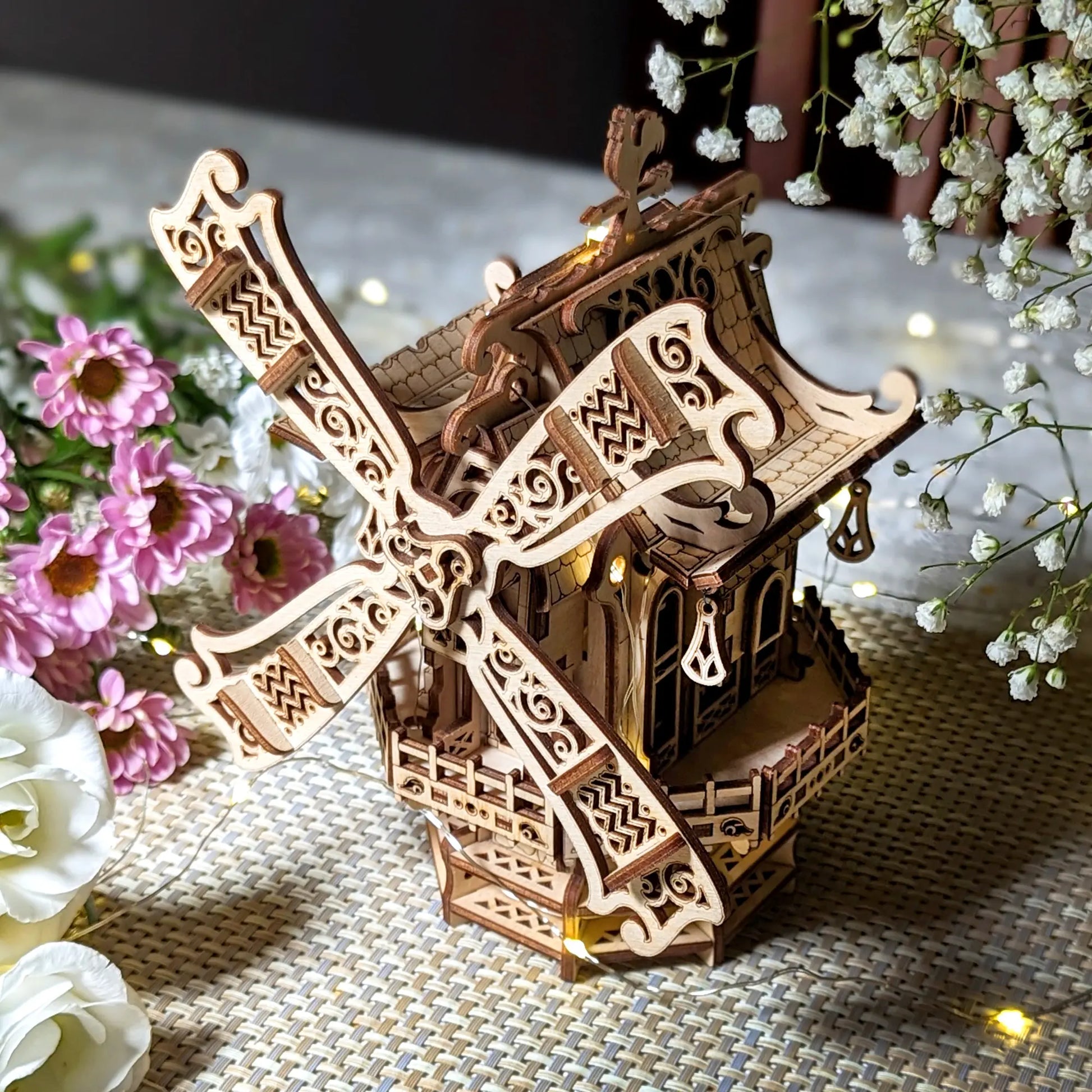 Wooden model of a windmill with decorative elements on a textured surface with flowers.