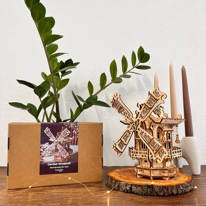 Wooden windmill model on a wooden base with a plant and candles in the background