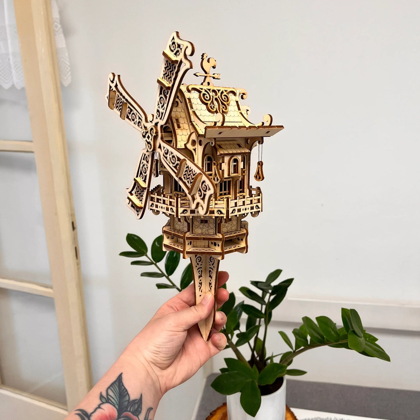 Hand holding a wooden model of a windmill against a neutral background