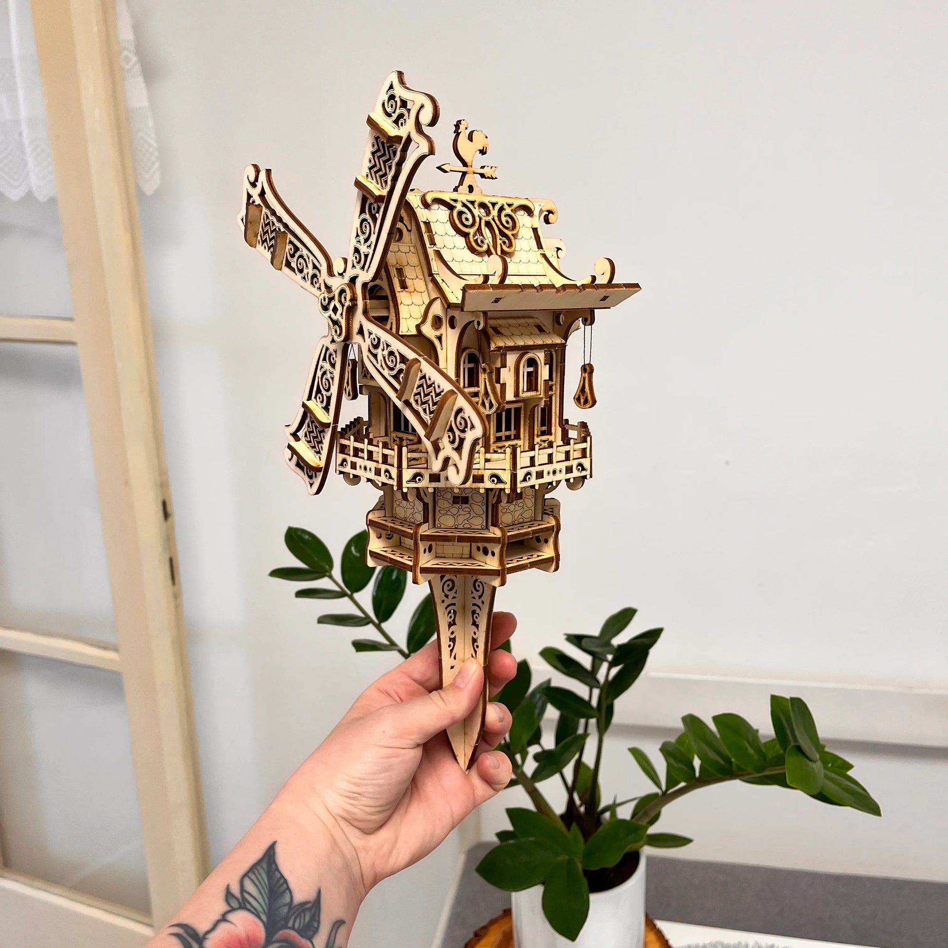 Hand holding a wooden model of a windmill against a neutral background