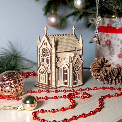 Small wooden church model among Christmas decorations including red beads, pine cones, and a tree.