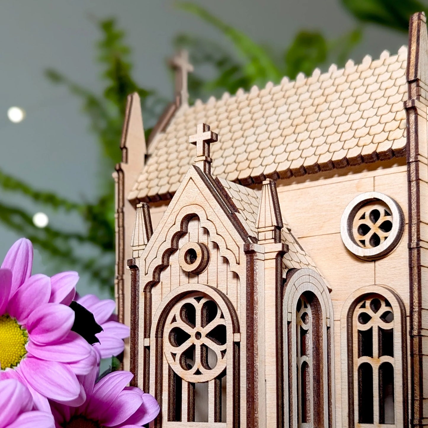 Wooden model of a gothic-style chapel with a purple flower in the foreground