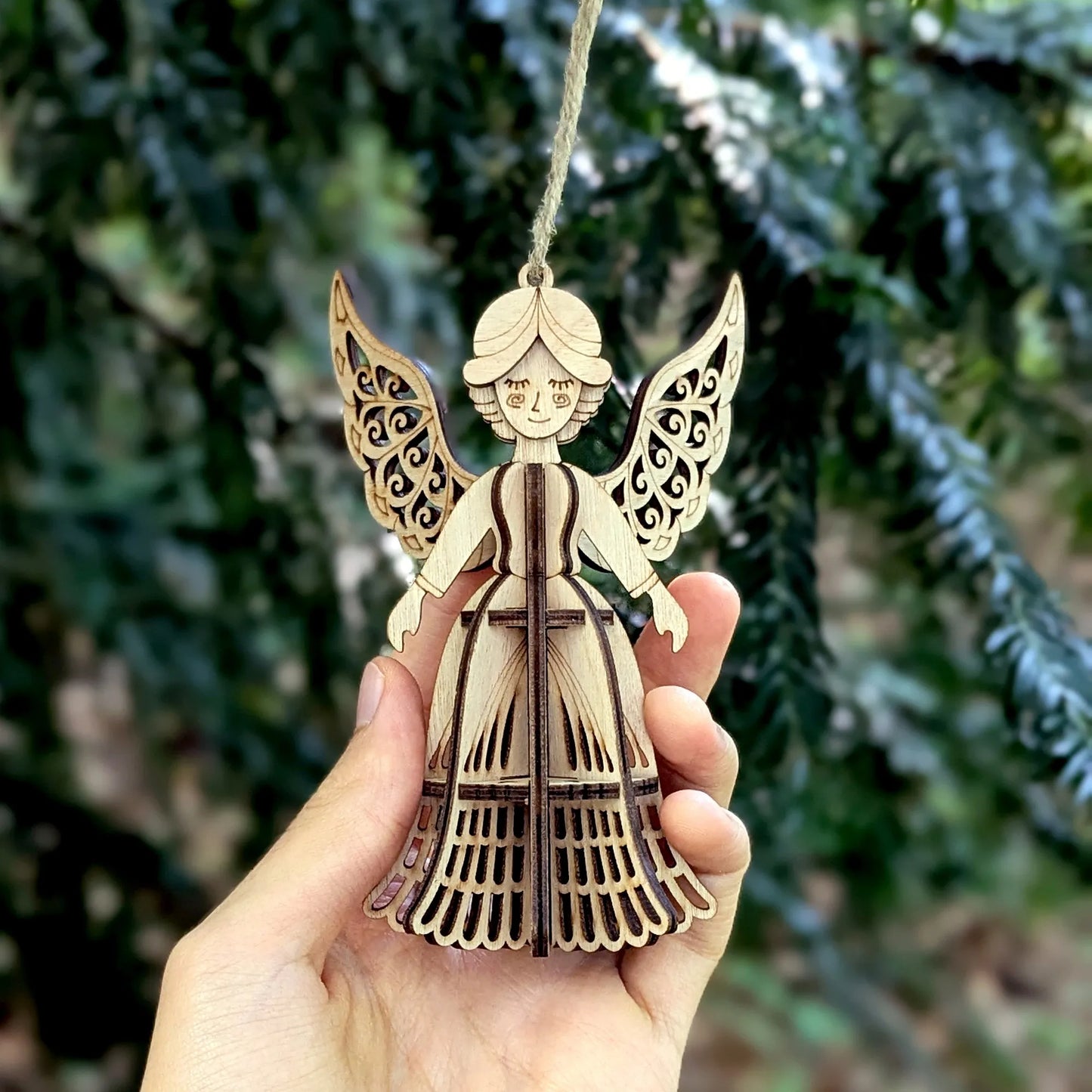 Wooden angel ornament held in a hand with a blurred green background