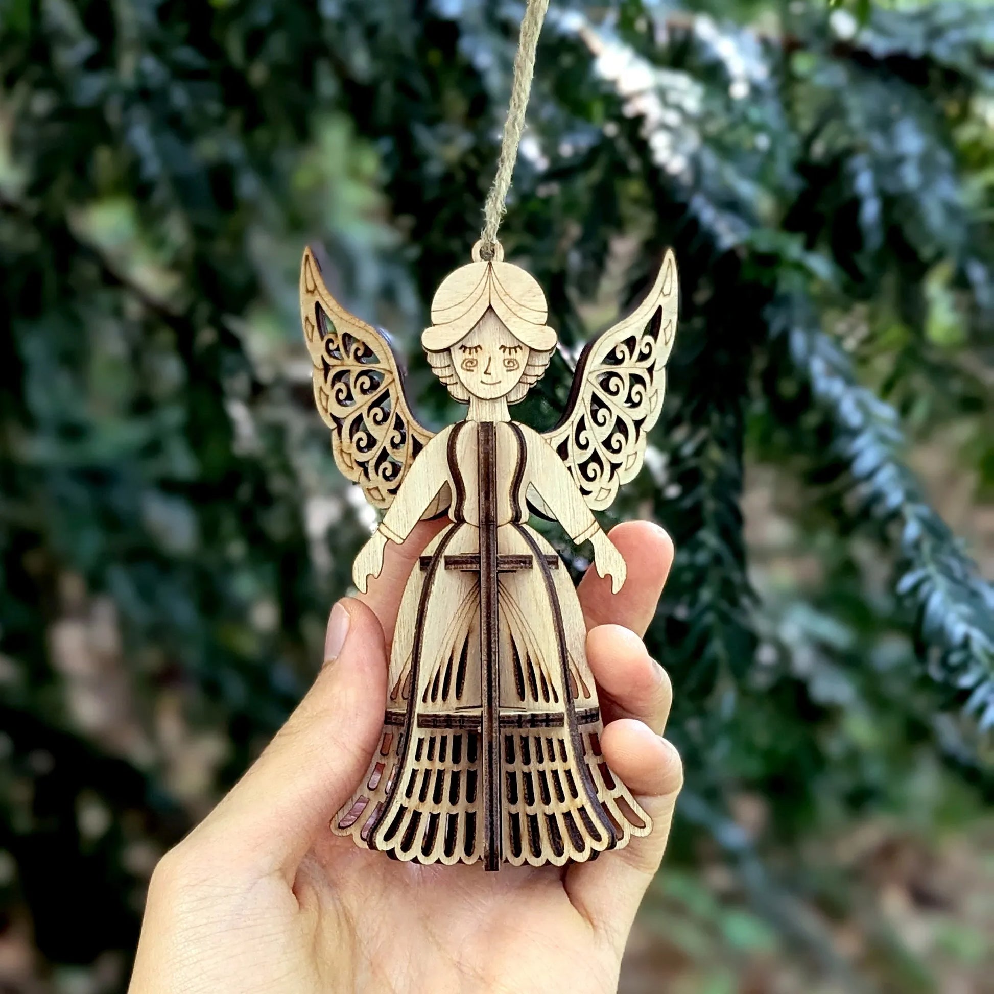 Wooden angel ornament held in a hand with a blurred green background