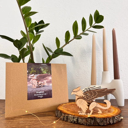 Wooden gryphon sculpture on a wooden base with a cardboard box and plant in the background.