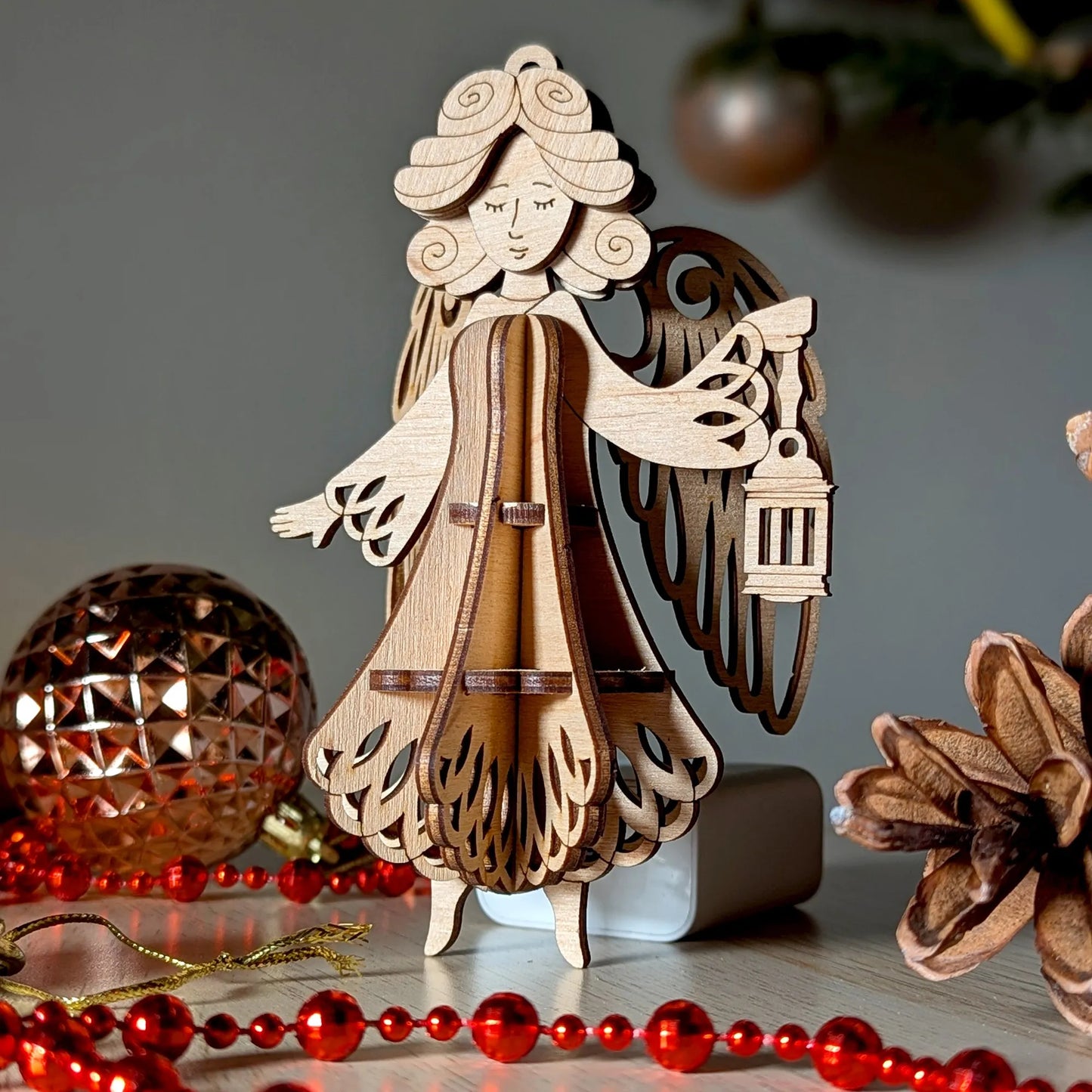 Wooden angel figurine with a lantern on a decorative background with red beads and a gold ornament.