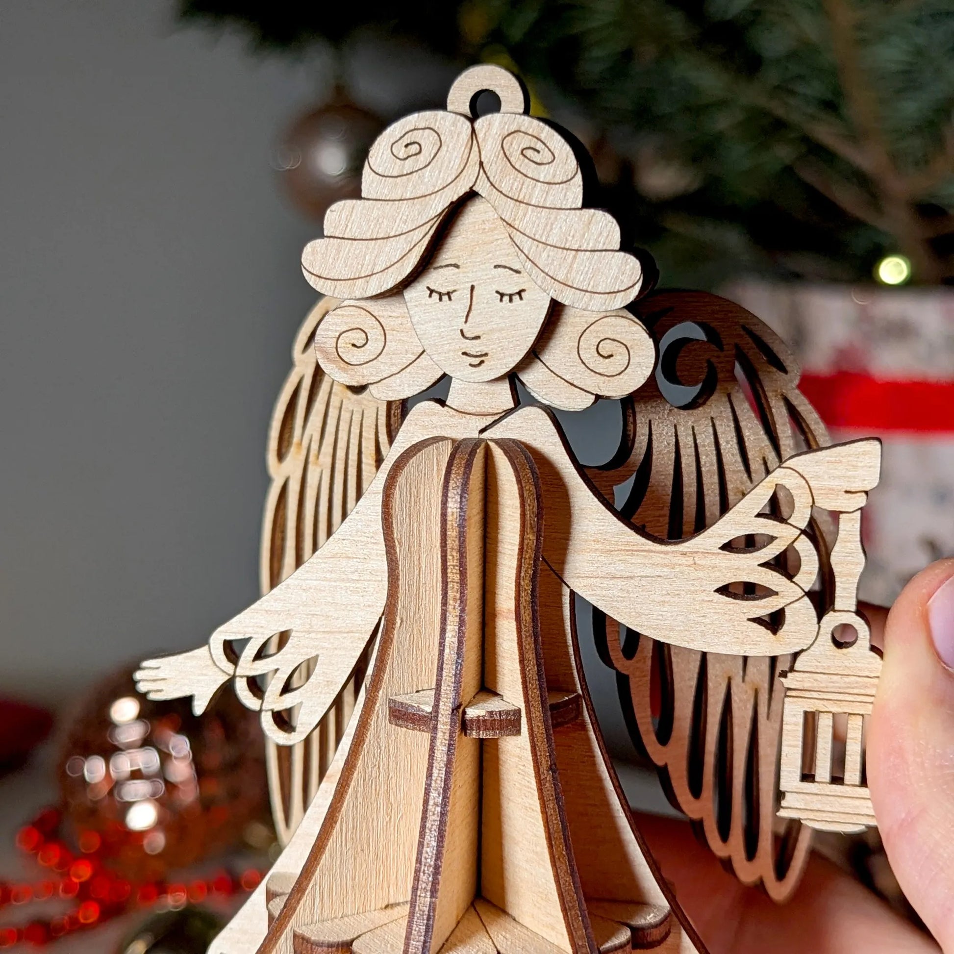 Wooden angel ornament held by a hand with Christmas decorations in the background