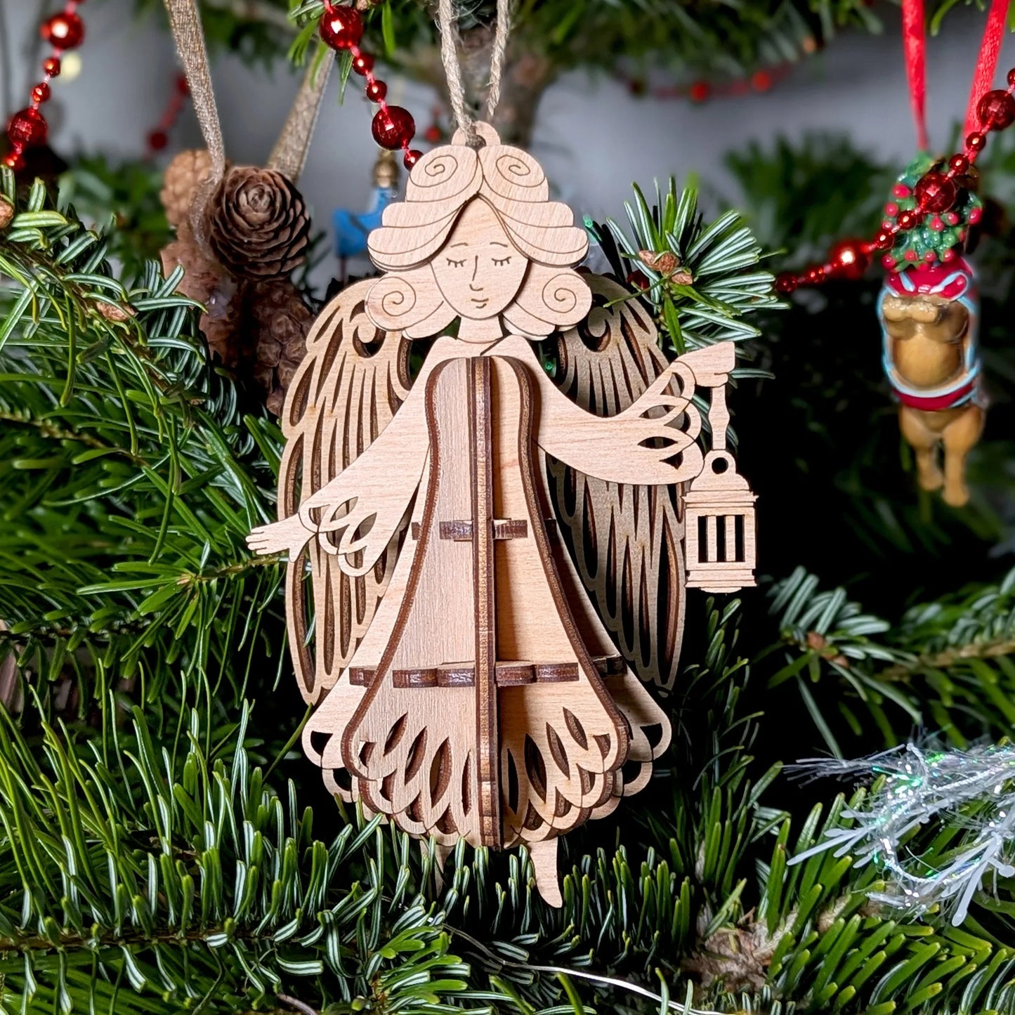 Wooden angel ornament hanging on a Christmas tree with red berries and pine cones.