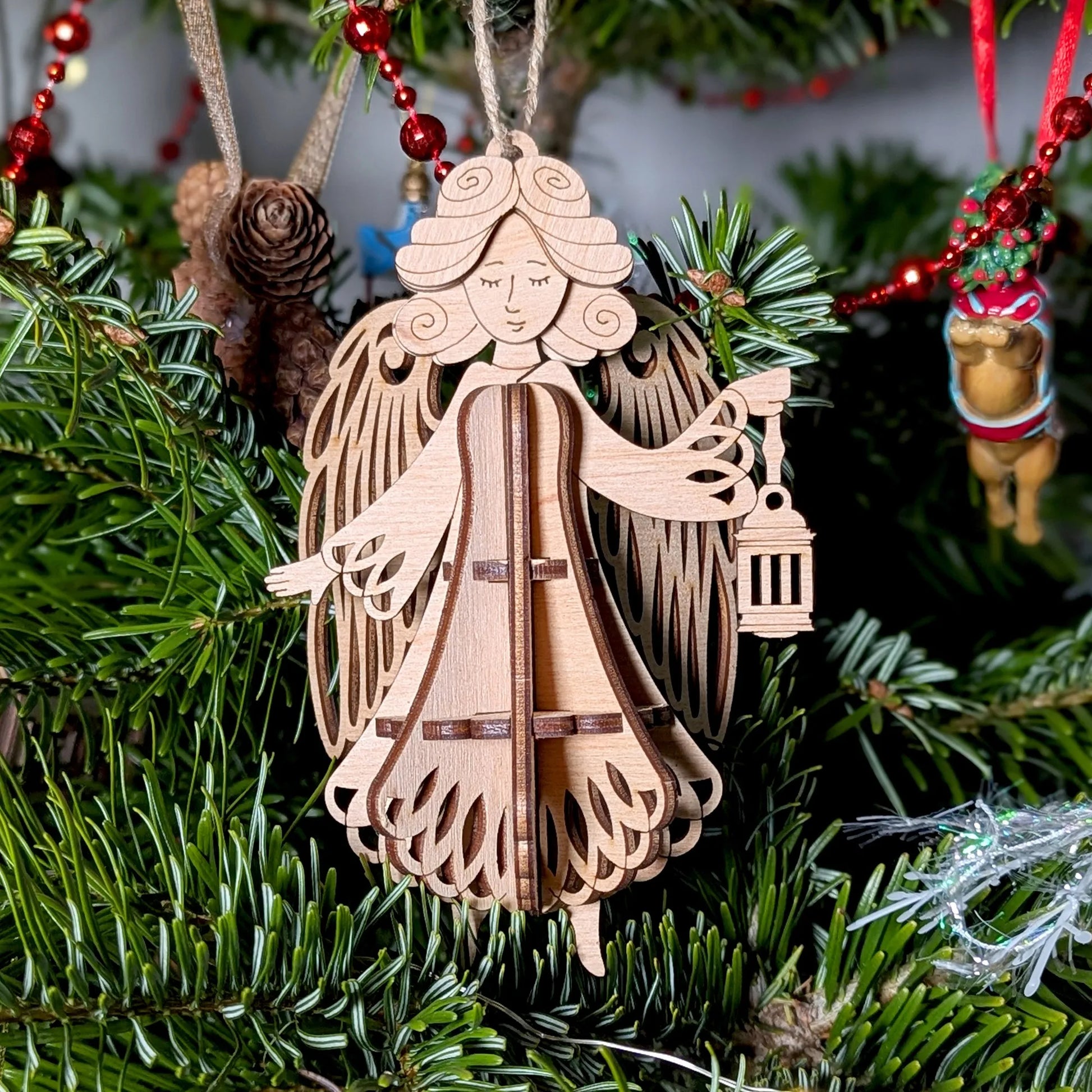 Wooden angel ornament hanging on a Christmas tree with red berries and pine cones.