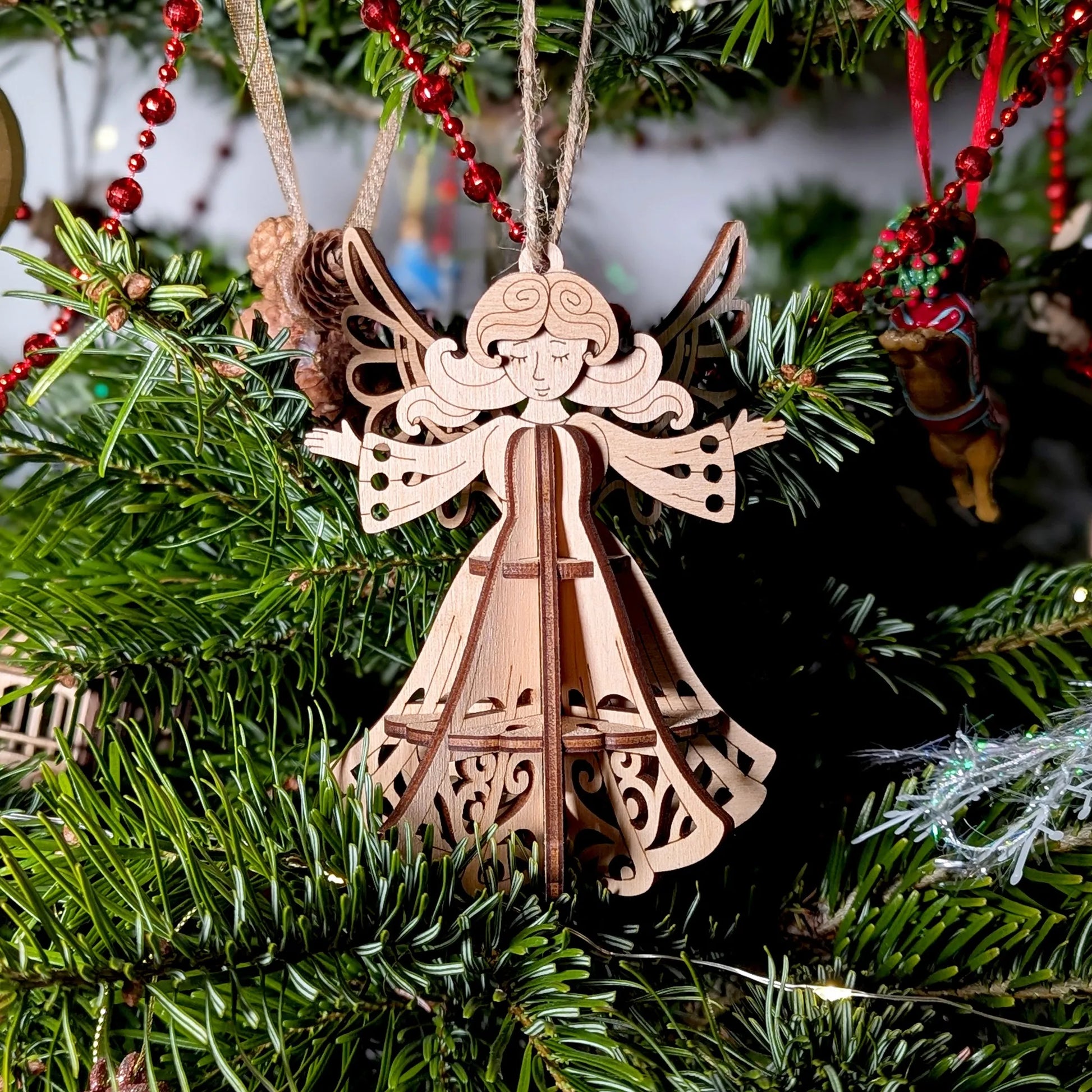 Wooden angel ornament hanging on a Christmas tree with green branches and red decorations.