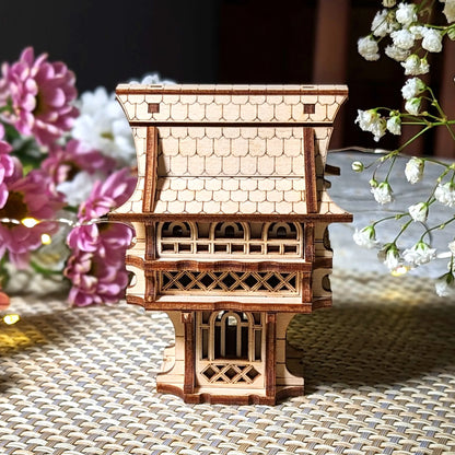 Wooden model of a pagoda on a woven surface with flowers in the background