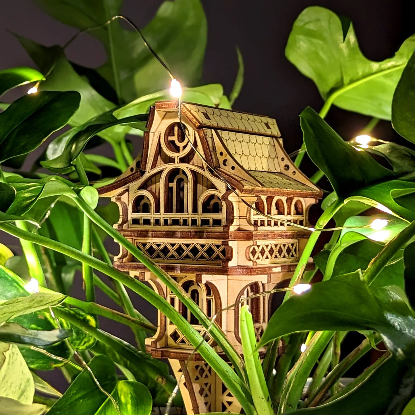 Wooden architectural model with lights embedded, surrounded by green leaves