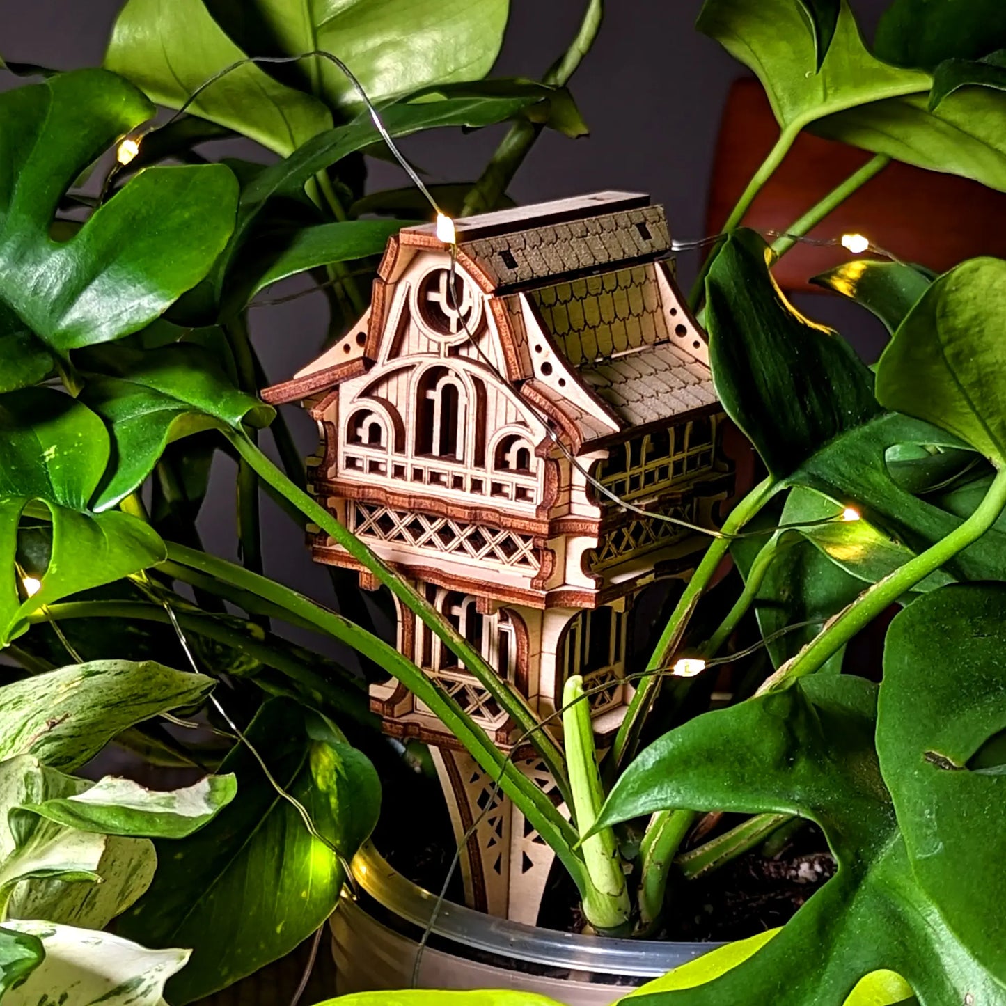 Wooden architectural model with lights embedded, surrounded by green leaves