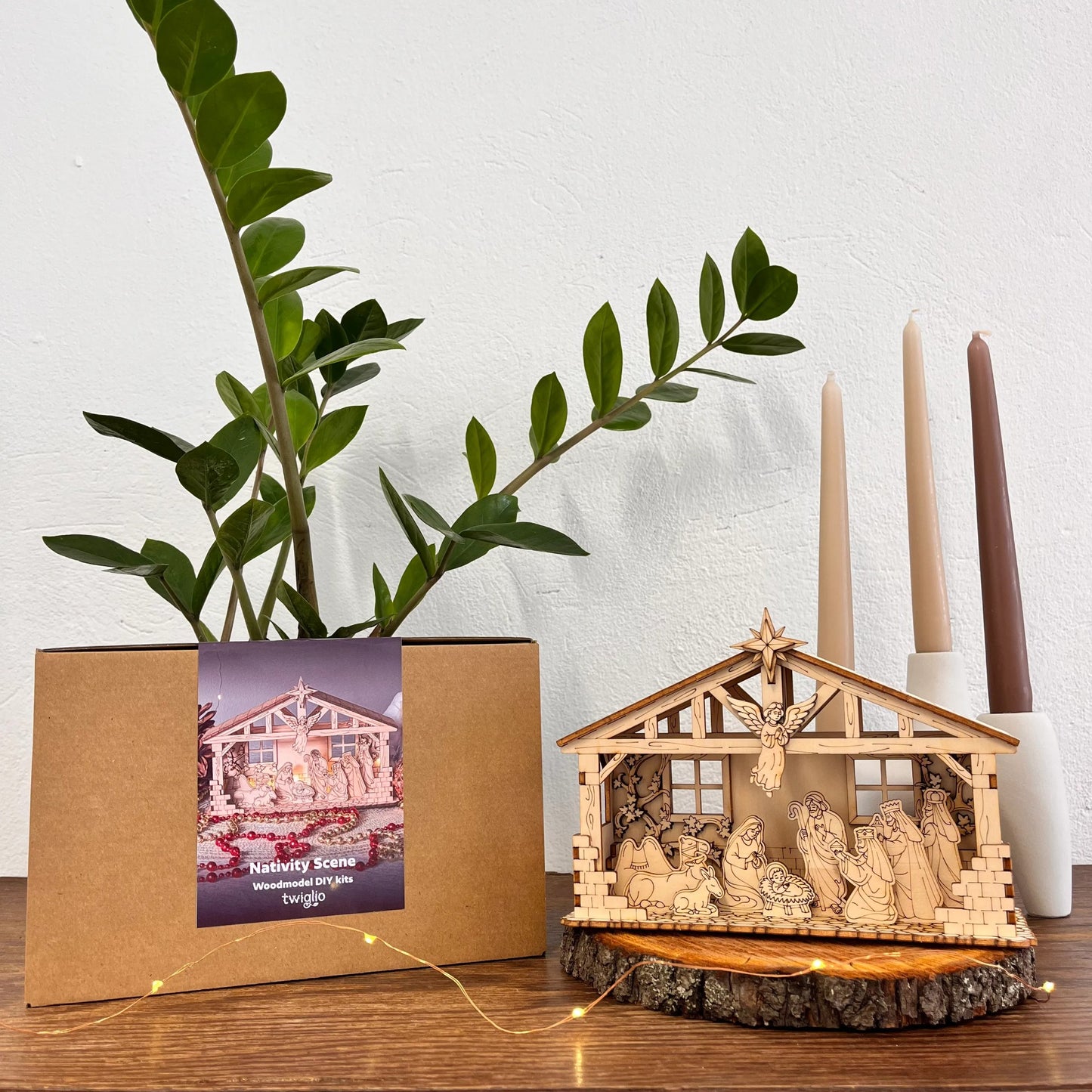 Nativity scene model with a plant and candles on a wooden surface