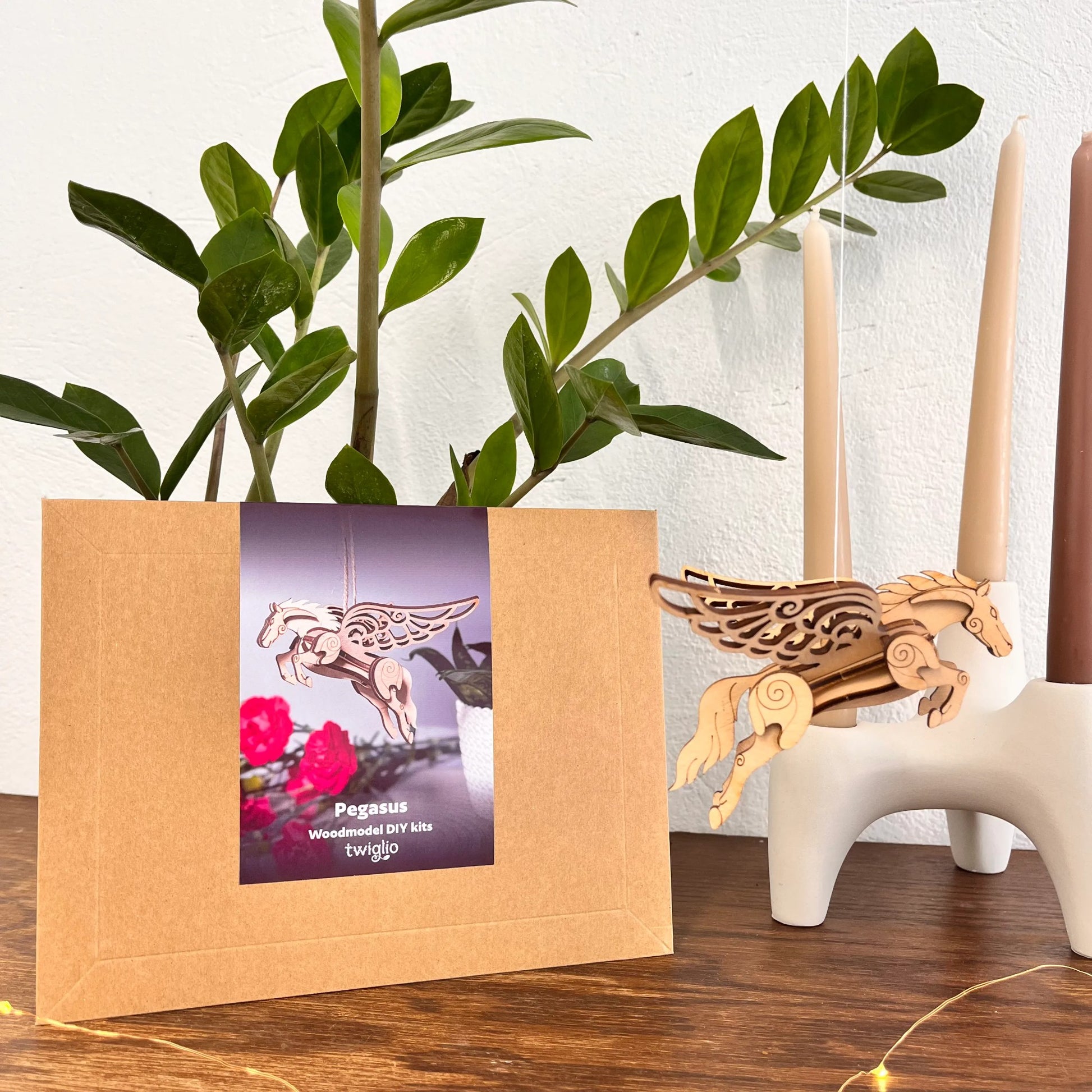 Wooden Pegasus model kit with packaging on a wooden surface, plant and candles in the background.