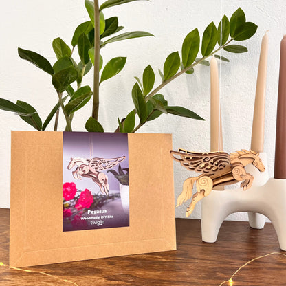 Wooden Pegasus model kit with packaging on a wooden surface, plant and candles in the background.