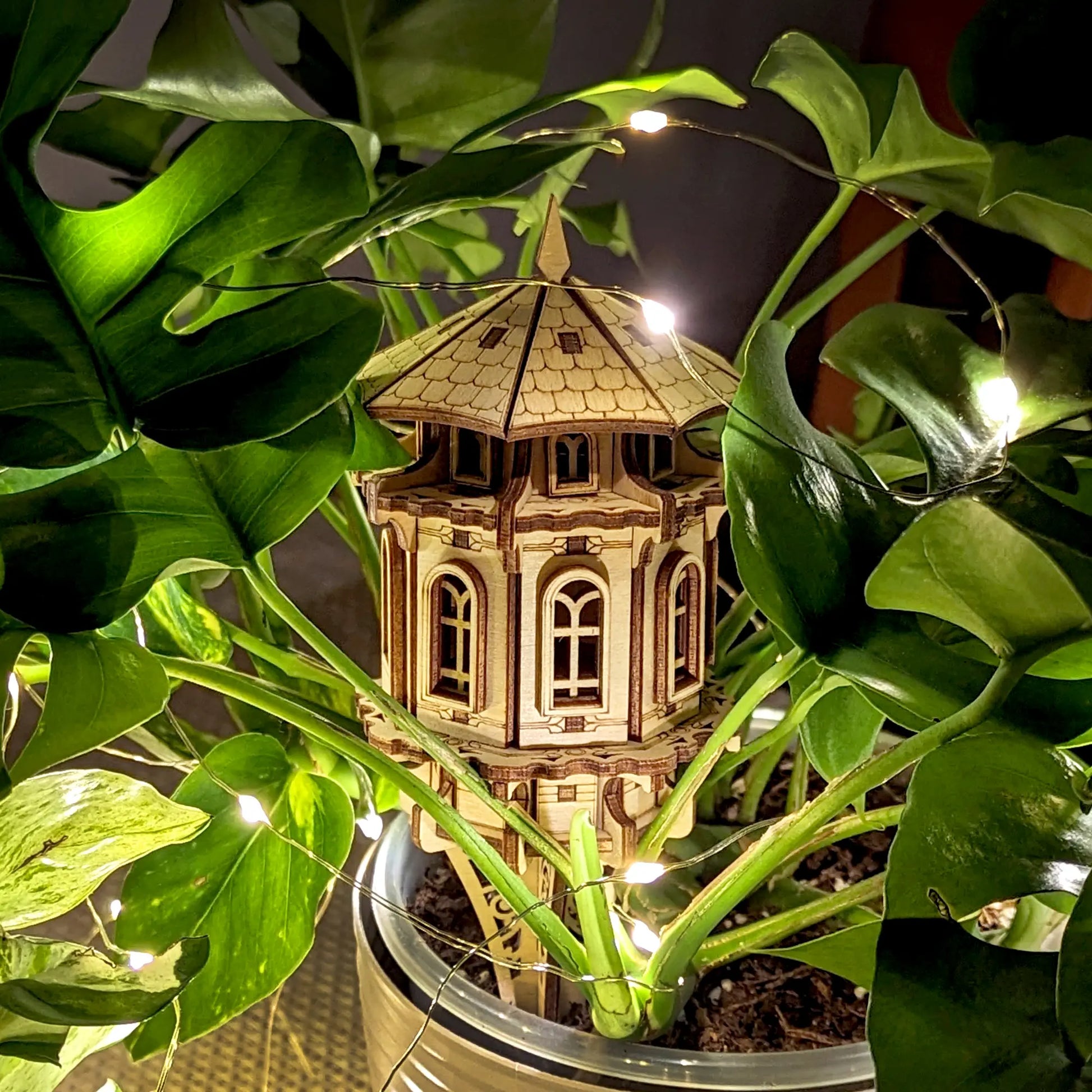 Small architectural model of a tower surrounded by green plants with string lights.