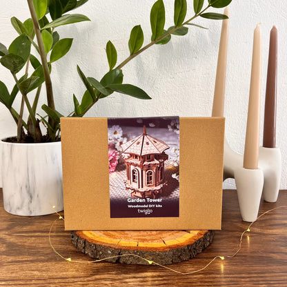 Wooden DIY kit packaging with garden tower design on a wooden surface with plants and candles in the background.