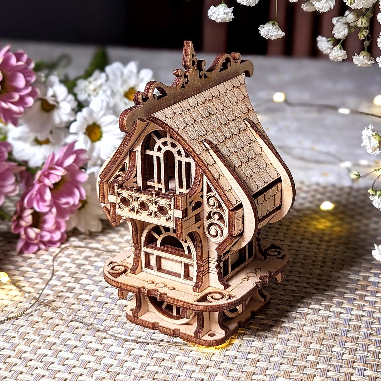 Wooden model of a decorative house on a textured surface with flowers in the background