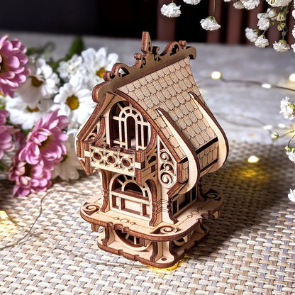 Wooden model of a decorative house on a textured surface with flowers in the background