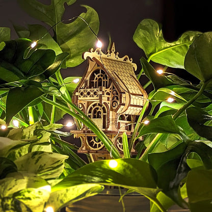 Wooden model of a house among green leaves with string lights